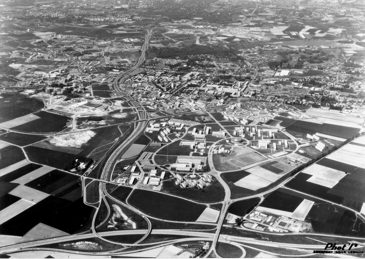 Vue aérienne depuis le sud, en mai 1977 : la cité scientifique, la desserte autoroutière, Le Triolo et plus loin les grands ensemble La Poste et La Résidence (AC Villeneuve-d'Ascq, Phot'R ; 9Fi2056).